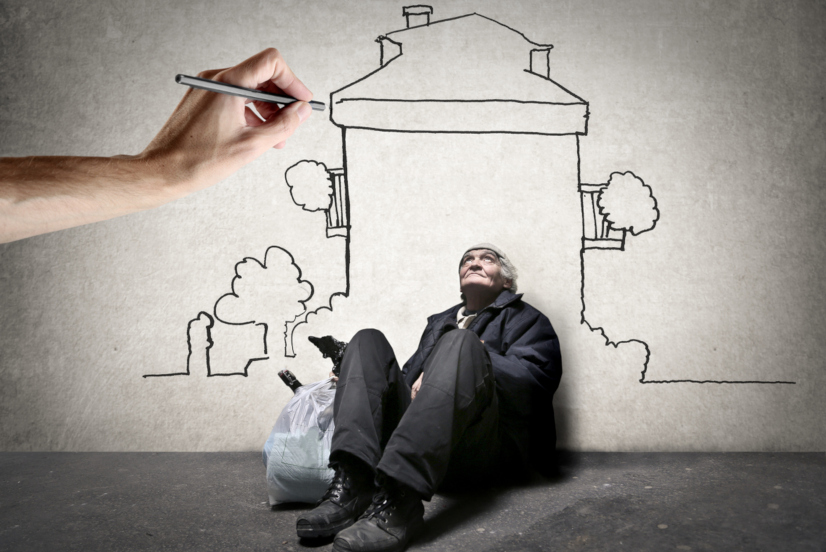 Homeless man is sitting on the ground while hand is drawing a house on the wall