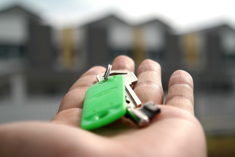 A hand holds out a set of keys on a green keyring.
